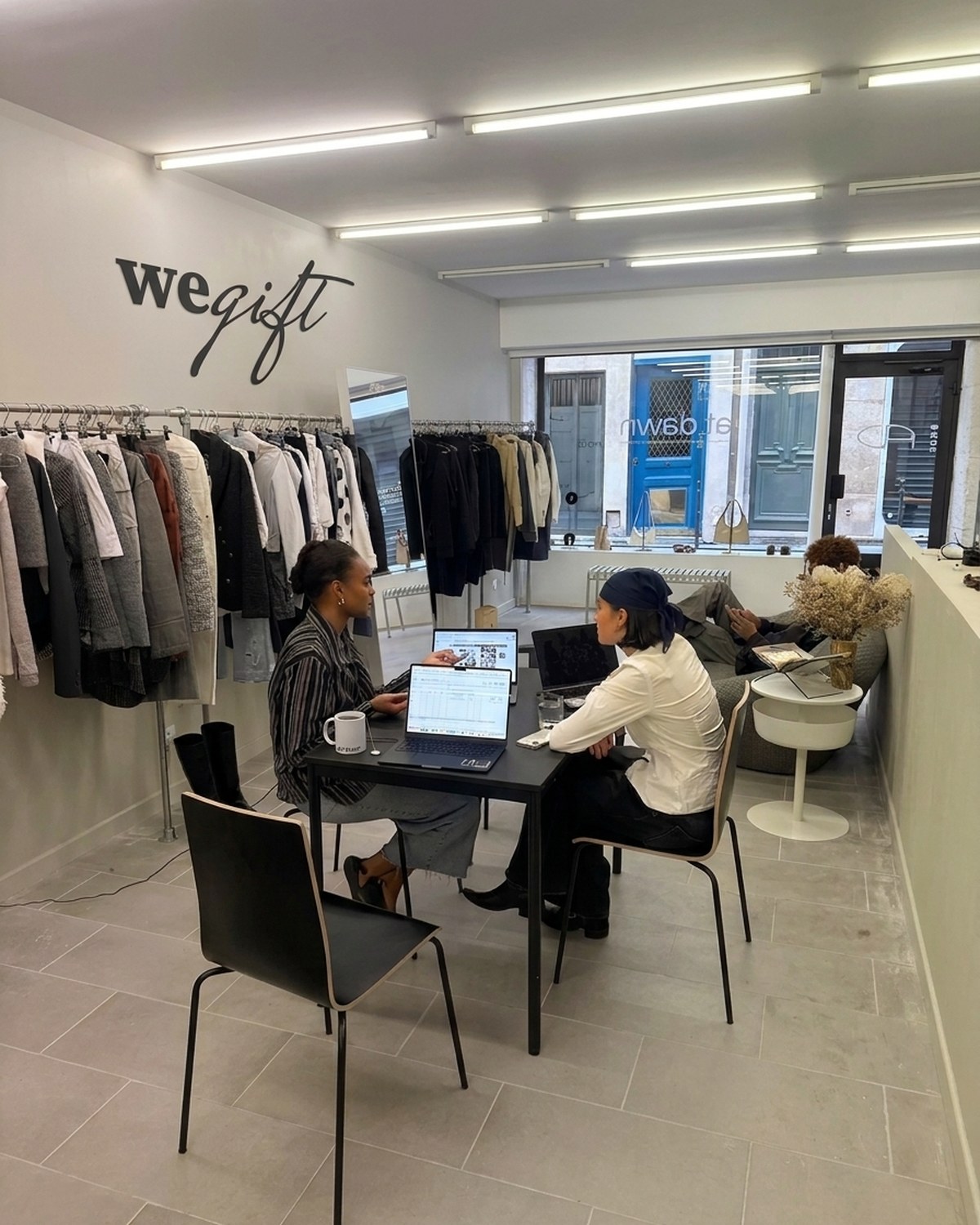Deux personnes en rendez-vous autour d'une table dans le showroom We Gift, portants de vêtements en arrière-plan.