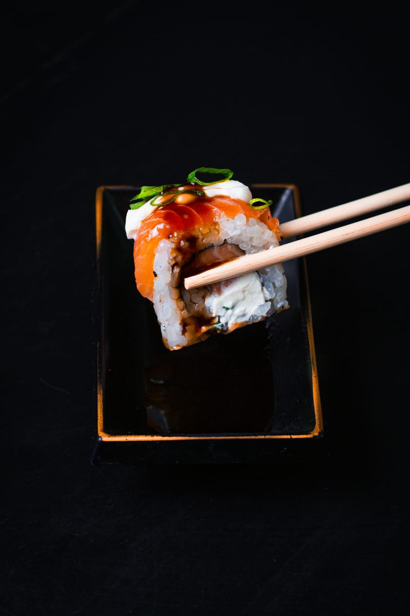 Makis tenus avec des baguettes au-dessus d'un plat noir avec sauce soja.