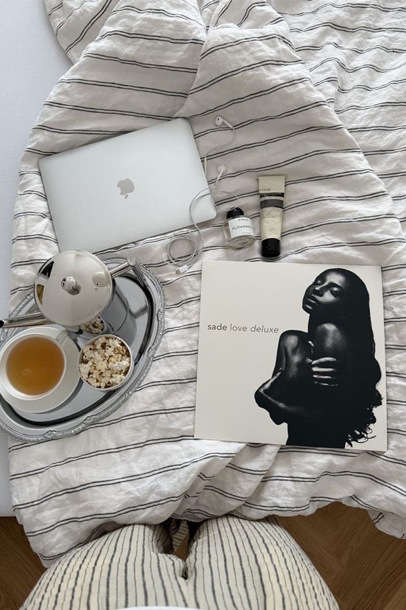Ordinateur portable, thé et vinyle posés sur un lit, ambiance cocooning.